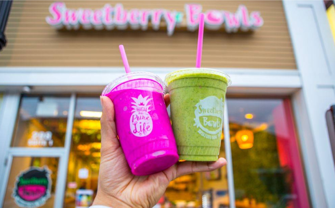 Two Sweetberry Bowls drinks held up outside a store